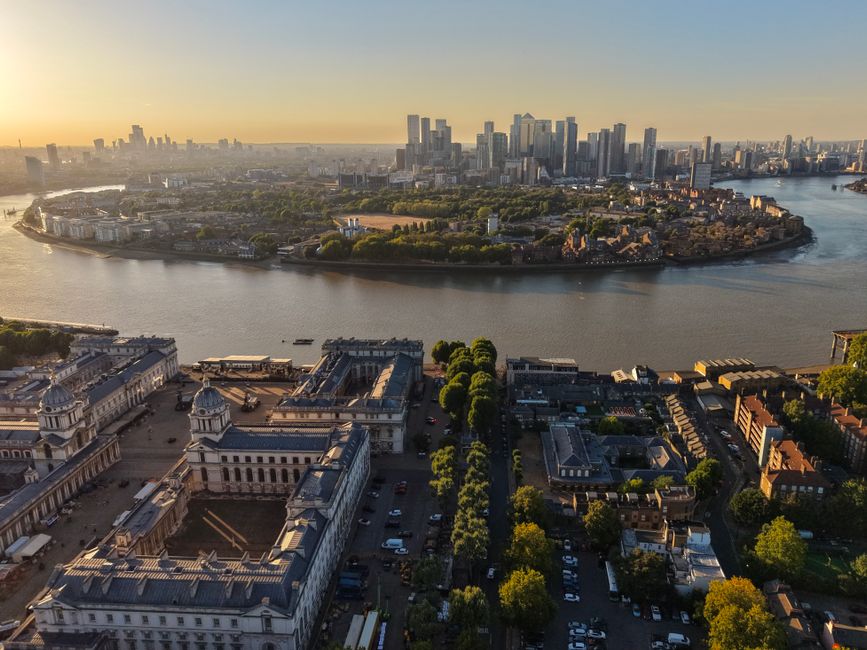 A wide panoramic view of the London skyline in the early evening, featuring modern high-rise office buildings and residential towers in the background, with a historic white mansion with classical arc